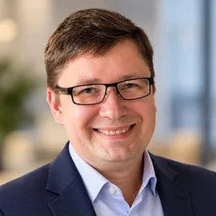 Portrait of Urmas Rehkalt, smiling, in a dark blazer and light blue shirt.
